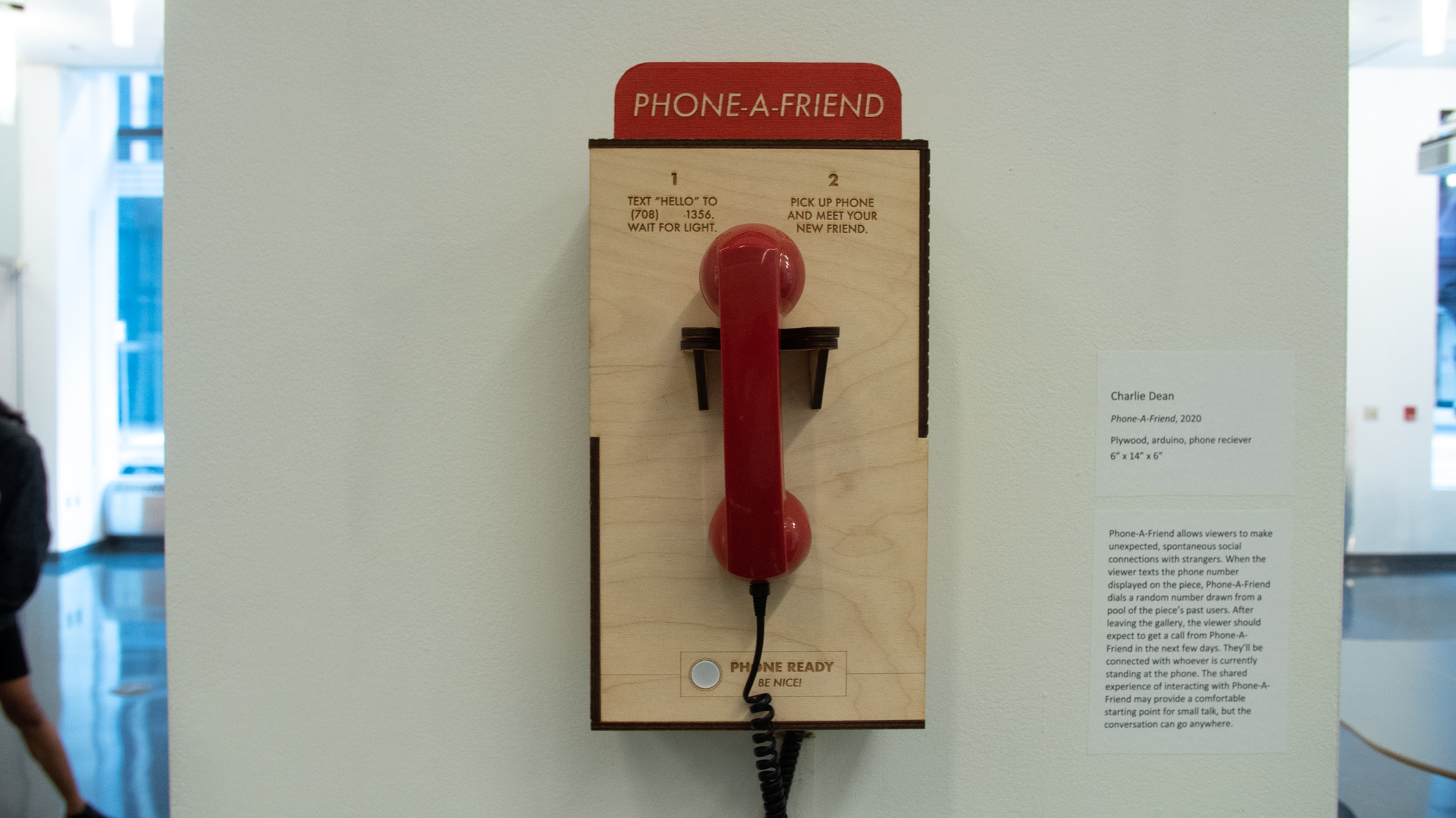 Phone-A-Friend - front view. A laser-engraved plywood box hanging on the wall. A sign reading Phone-A-Friend is mounted to the top of the box. A red plastic handset is hanging from the front of the box.